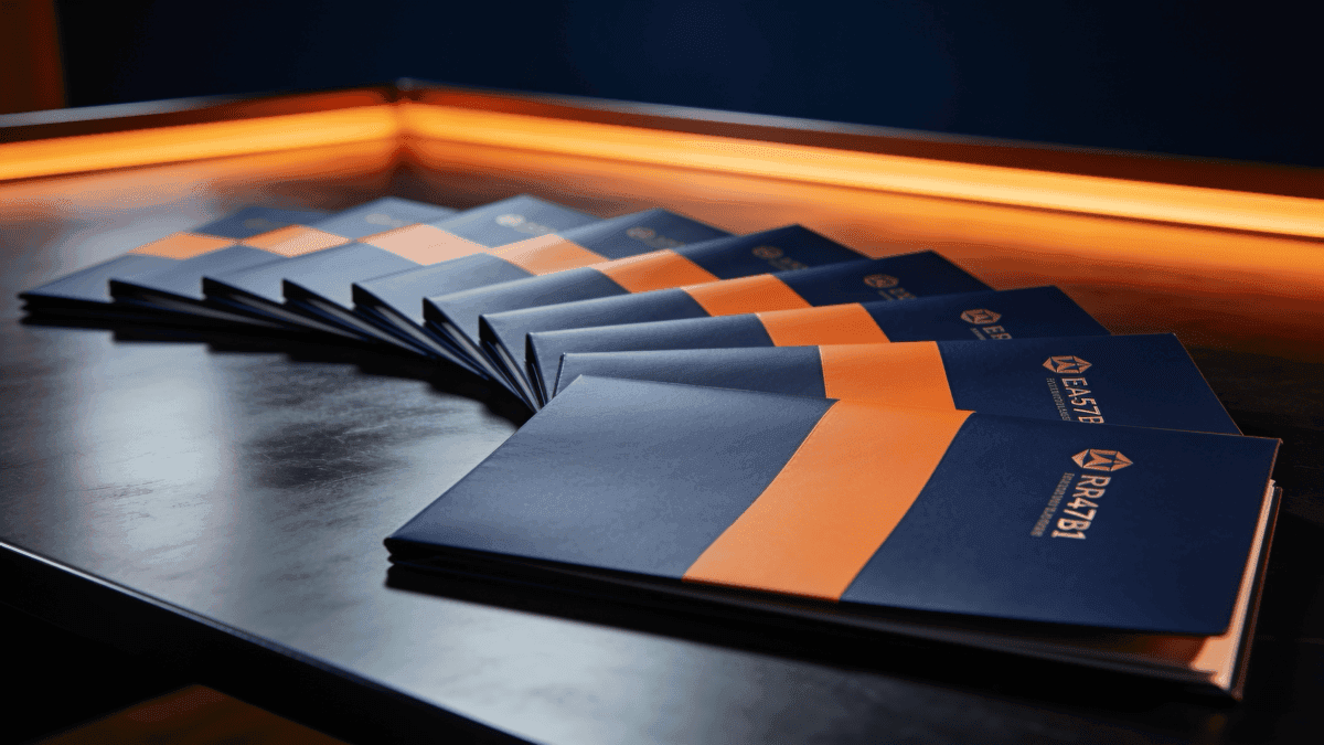 A neat row of identical branded report folders fanning out across a desk, deep navy with warm orange light, suggesting a service that scales per customer